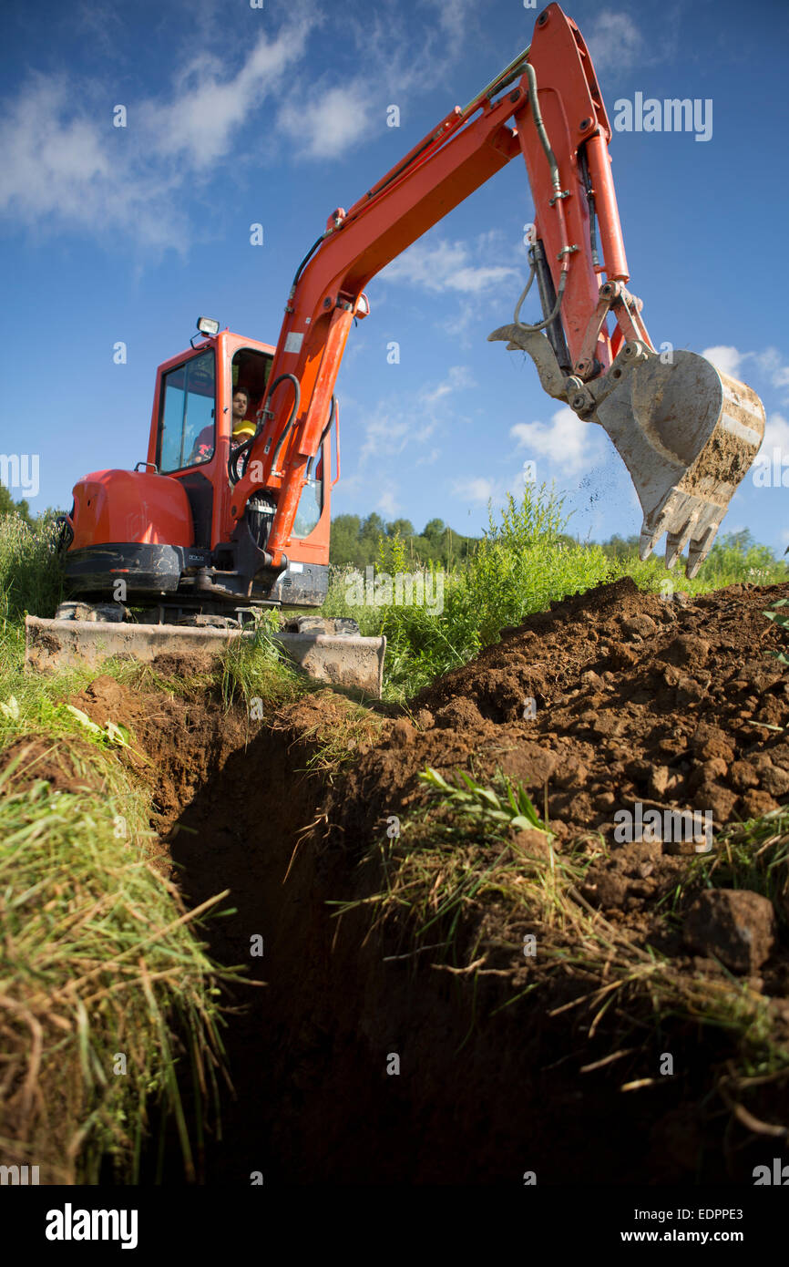 Man and kid digging a trench with a backhoe Stock Photo