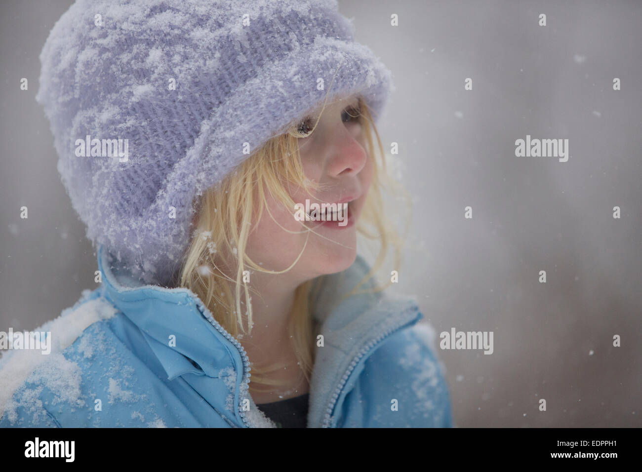 Little girl in snowy winter hat and coat smiling at the snowfall Stock Photo