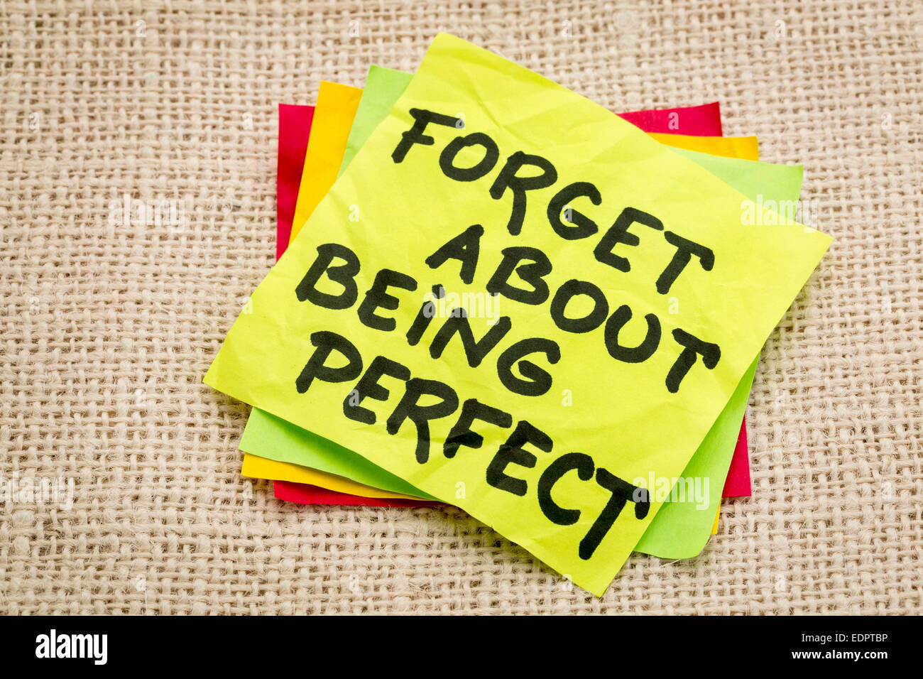 forget about being perfect - advice on a sticky note against burlap canvas Stock Photo