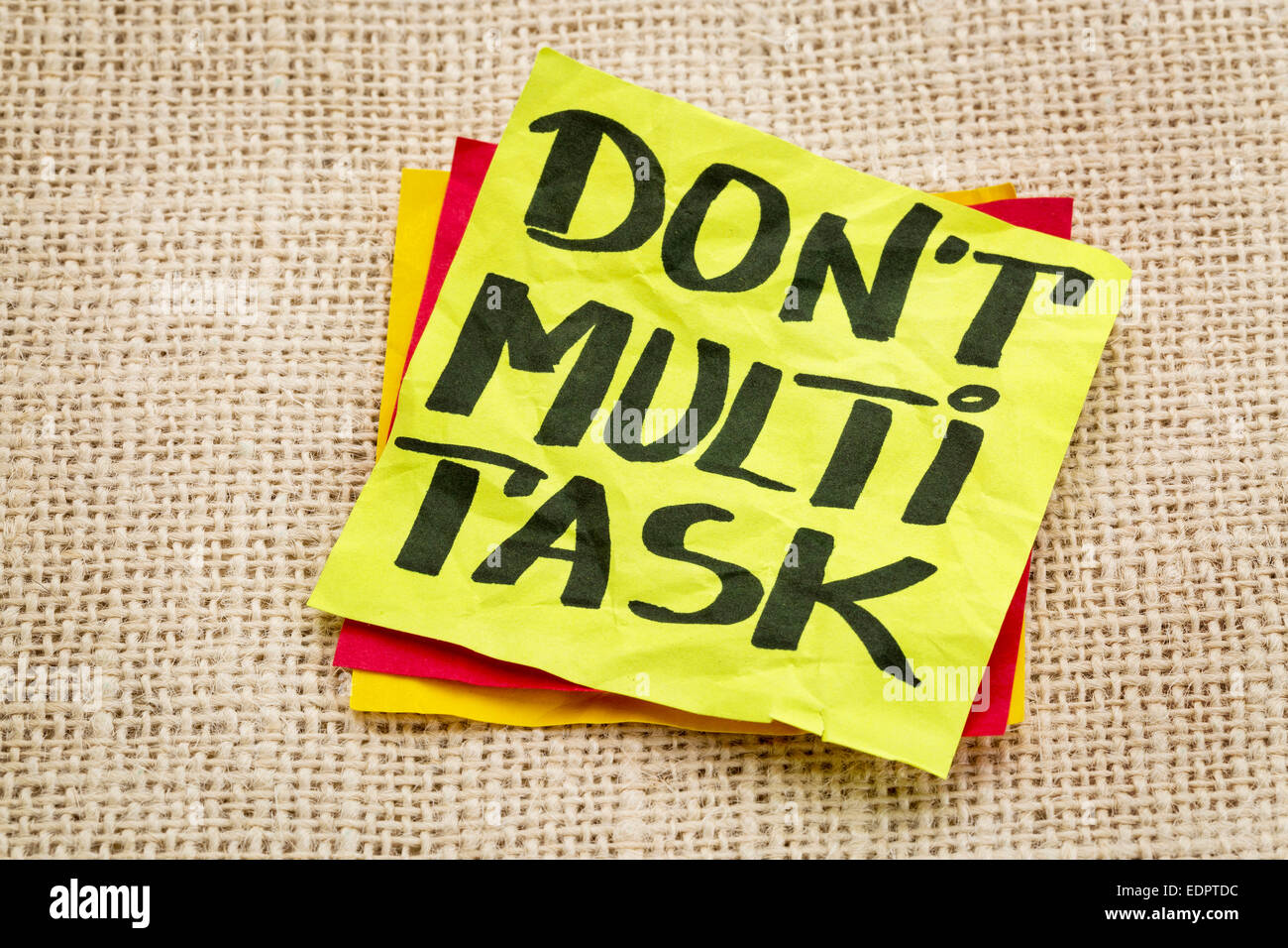 do not multitask - efficiency advice on a sticky note against burlap canvas Stock Photo