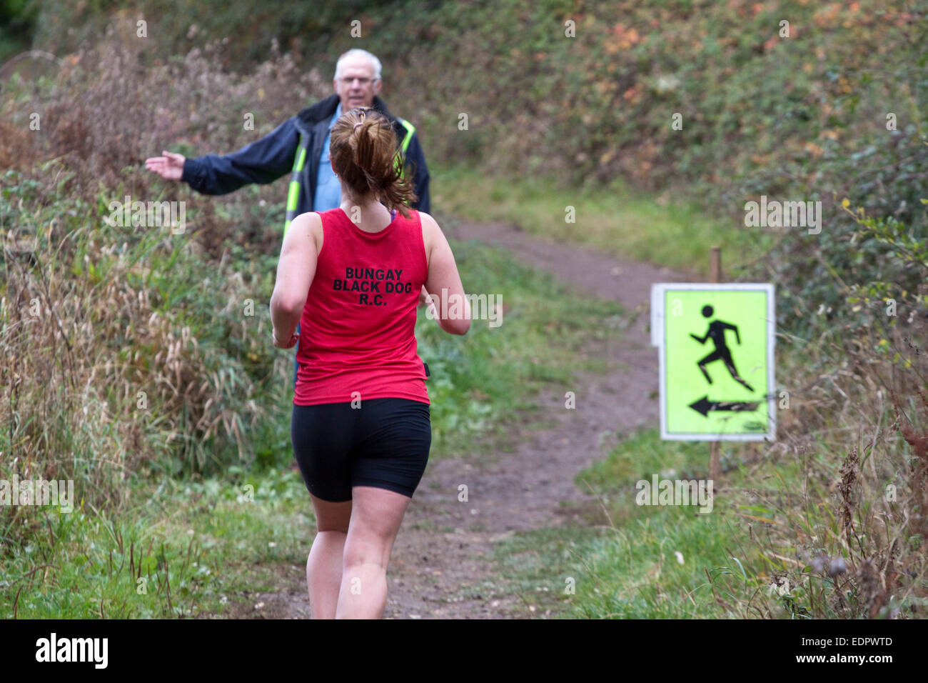 Woman runner in red top approaches a marshaled turn in a cross country race. Stock Photo