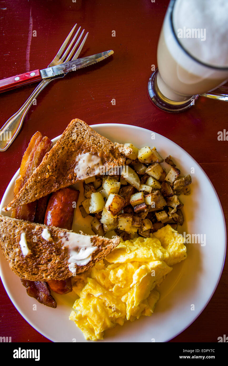 A plate of breakfast food including toast, bacon, potatoes and eggs with a latte on the side at a restaurant in California. Stock Photo