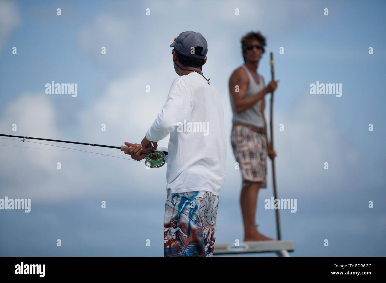 fisherman reels fly rod while man in back uses pole to stear boat Stock Photo