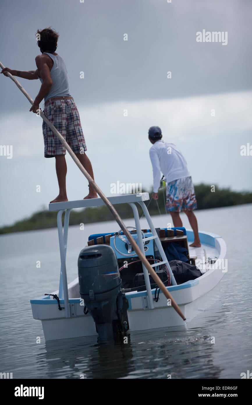 rear view of flats boat shows man with pole and fisherman on bow Stock