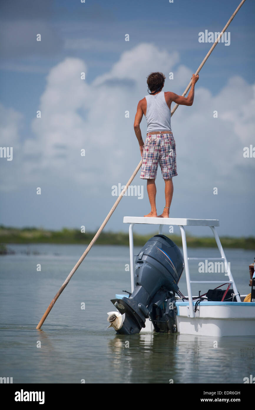 a man standing on flats boat platform uses pole to push through