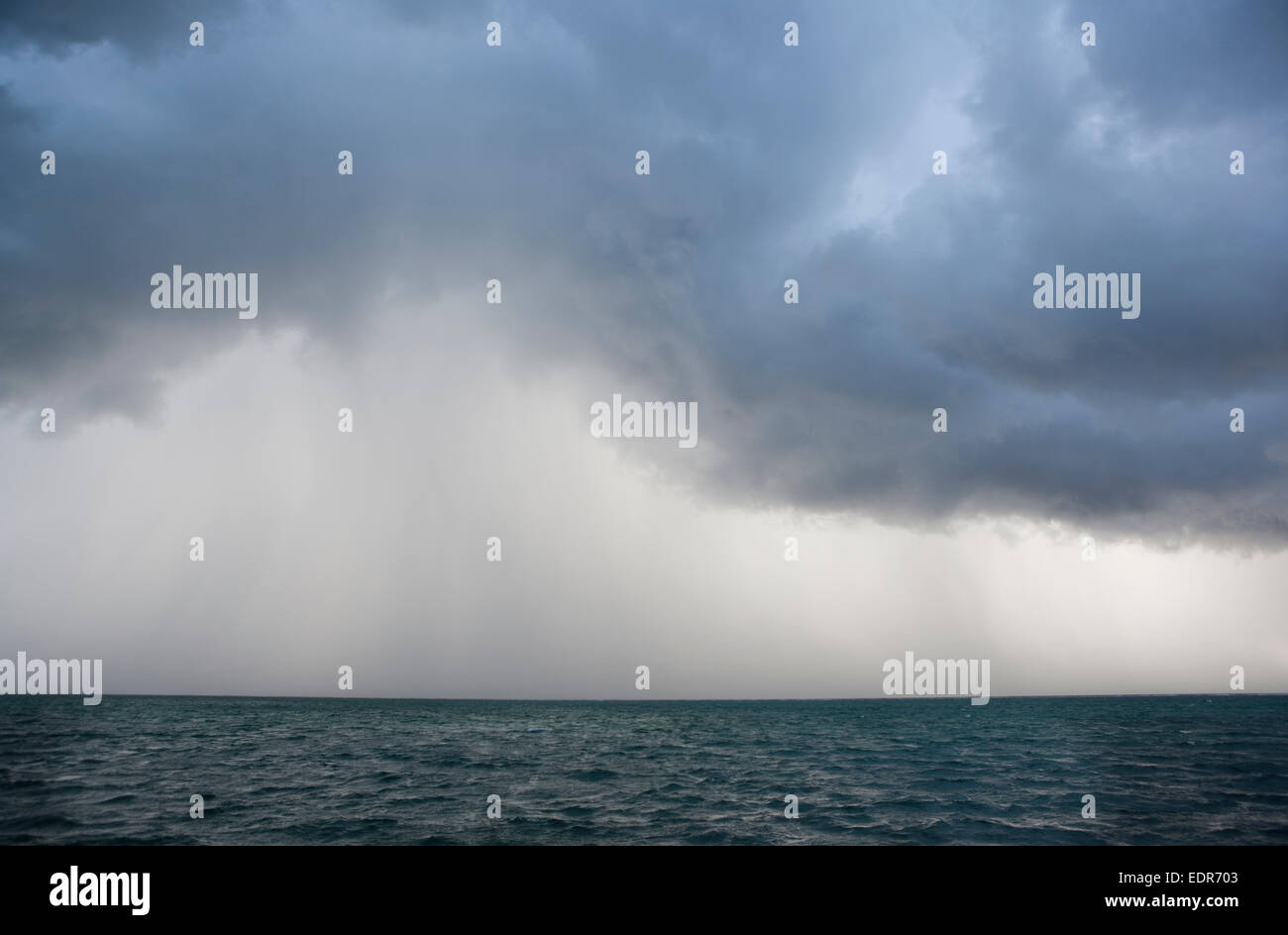 a view of an ocean storm with menacing clouds and rain showering below Stock Photo