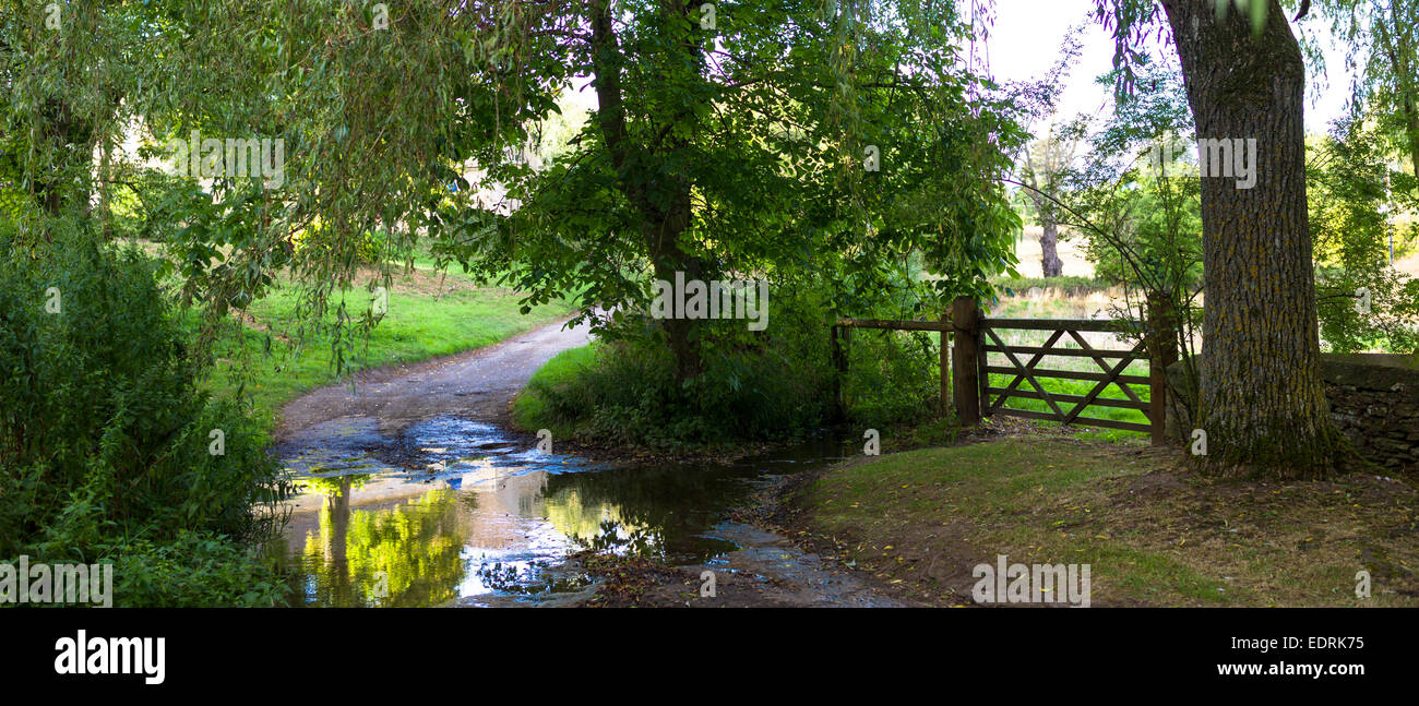 Stream ford crosses country lane rural scene in Swinbrook in The Cotswolds, England, United Kingdom Stock Photo