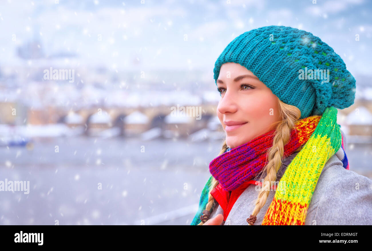 Portrait of cute happy woman enjoy snowfall in beautiful Prague city, wearing stylish colorful hat and scarf, enjoying winter Stock Photo