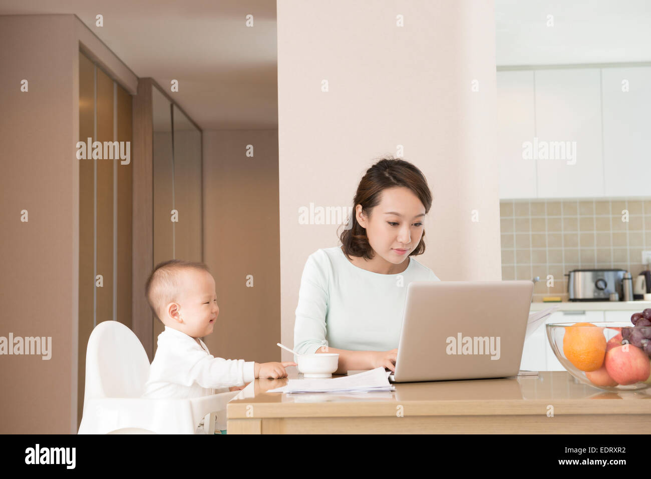 Young mother working while feeding baby boy Stock Photo