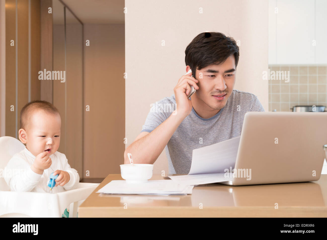 Young father working while feeding baby boy Stock Photo