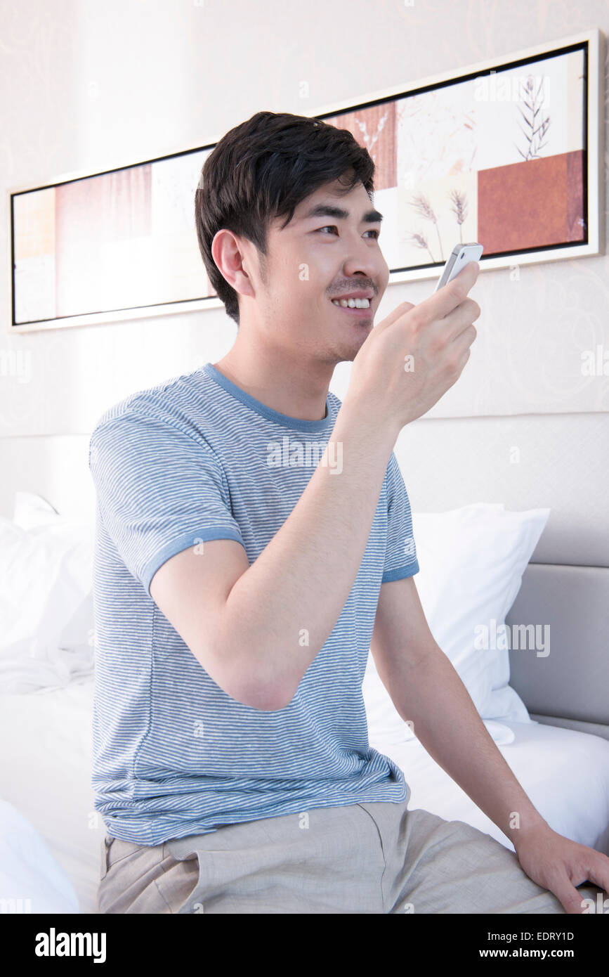 Young man sending voice message in bed Stock Photo