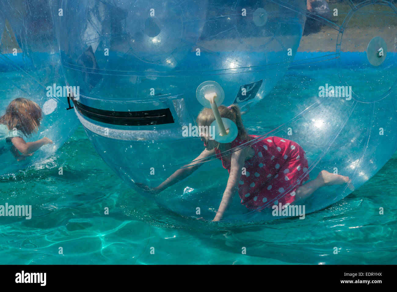 Little girls running in inflatable giant plastic ball floating on water