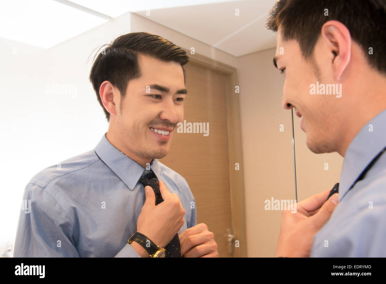 Young man putting on tie in front of mirror Stock Photo Alamy