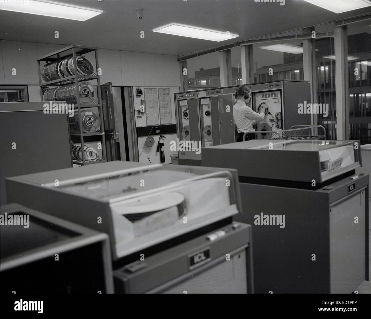 1968, historical, machine room with ICL computer hardware or mainframes, with a technician or engineer or operator working on a tape or recording deck. Stock Photo