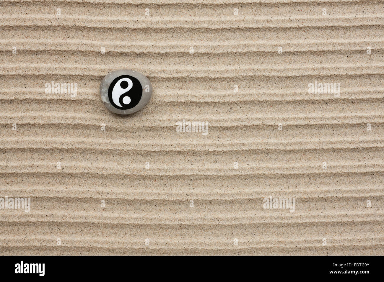 Stone with a yinyang lies on the sand as the background Stock Photo