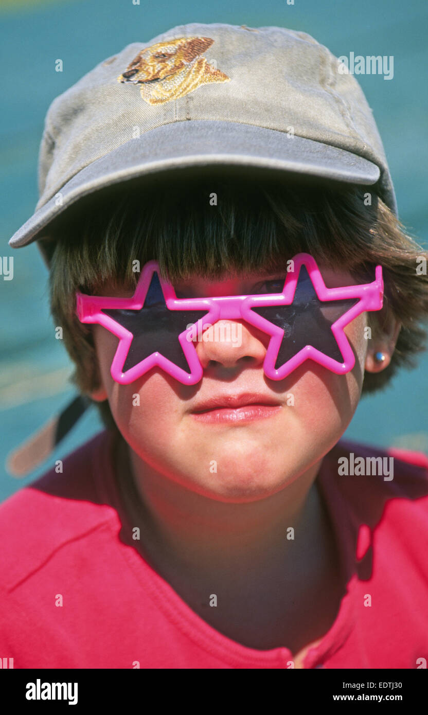 A ten year old girl wearing a baseball cap and plastic sunglasses looking like a tomboy. Stock Photo