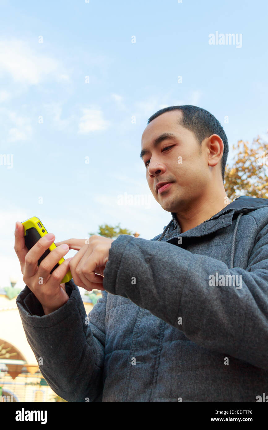 handsome thai man with gray coat is playing mobile phone Stock Photo