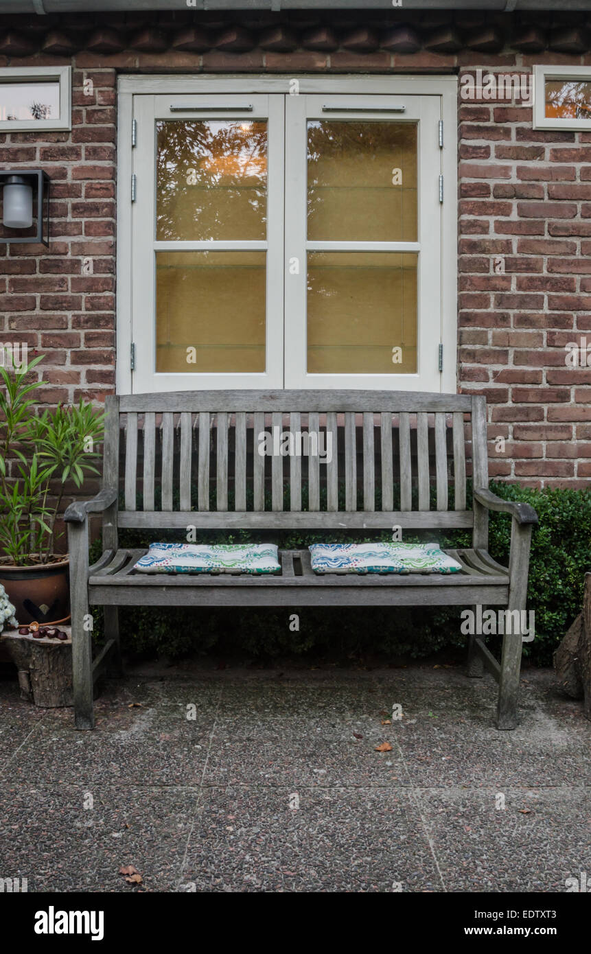 An outdoor garden seating area with a wooden bench and cushions Stock Photo