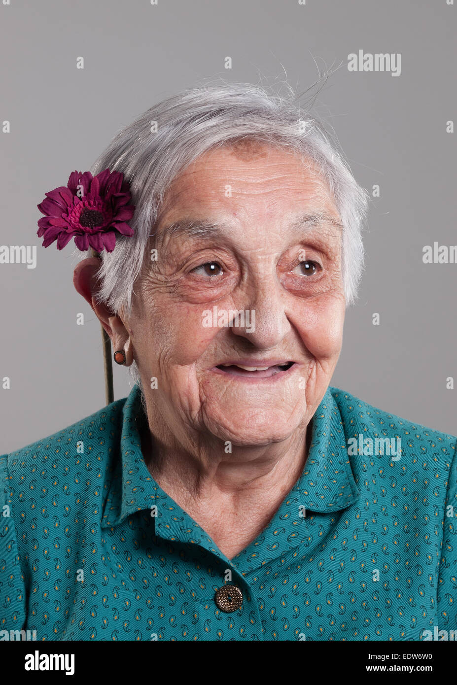 Elderly woman similing with a flower in her ear in a studio shot. Stock Photo