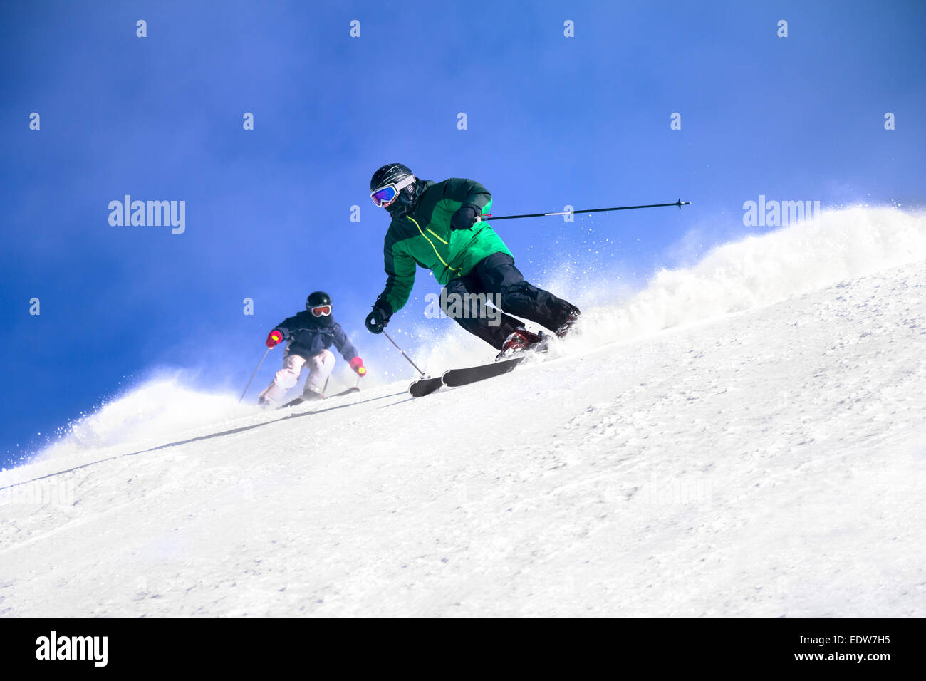 Two Skiers skiing downhill in high mountains and sunny day Stock Photo