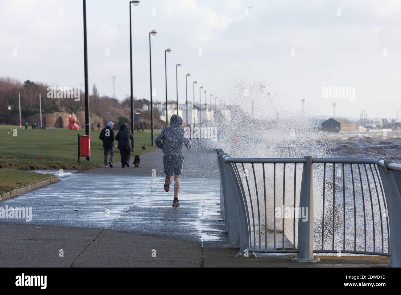 Liverpool, Merseyside, UK. 10th January, 2015. A jogger is soaked by waves whipped up by strong winds on Otterspool Promenade, Liverpool Credit:  Adam Vaughan/Alamy Live News Stock Photo
