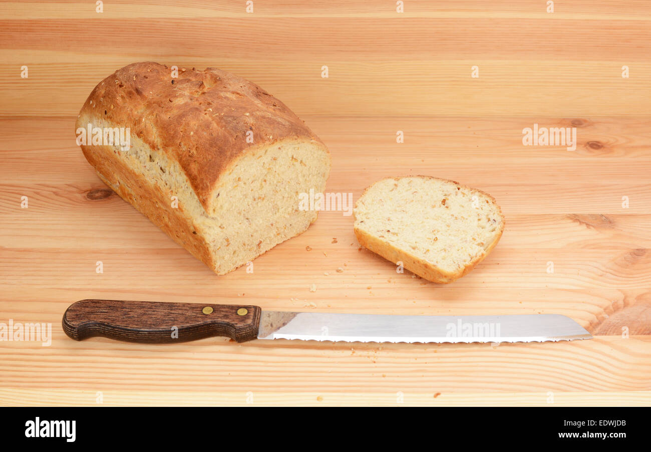 Bread knife with freshly sliced loaf of oat and linseed bread on a wooden table Stock Photo