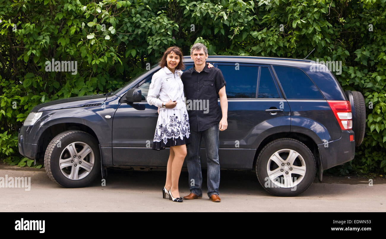Young man and woman standing near black car (model Suzuki grand vitara). Stock Photo