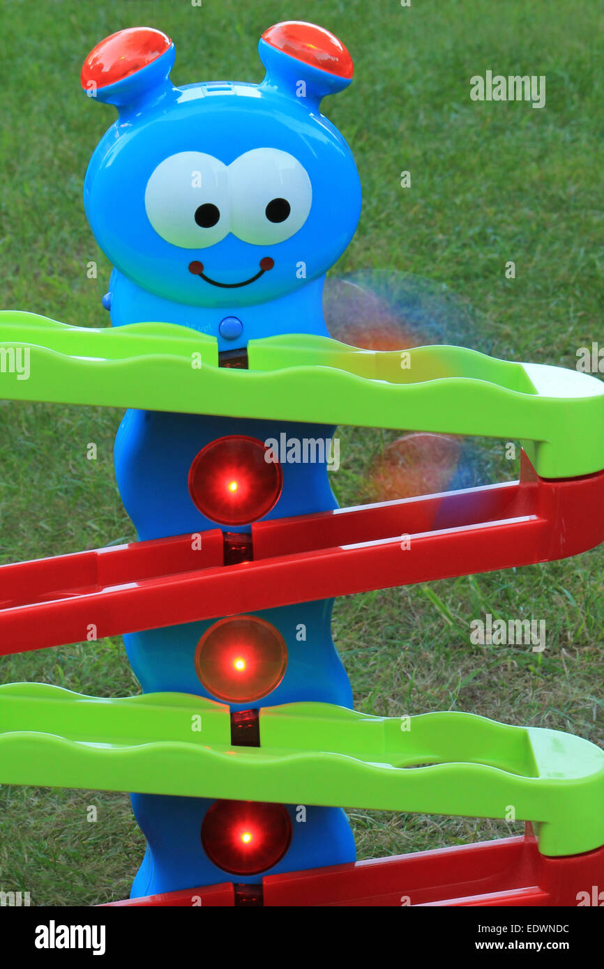 Colourful caterpillar toddler toy on a lawn lit up and flashing as a ball is captured mid-motion, falling down the ramps. Stock Photo