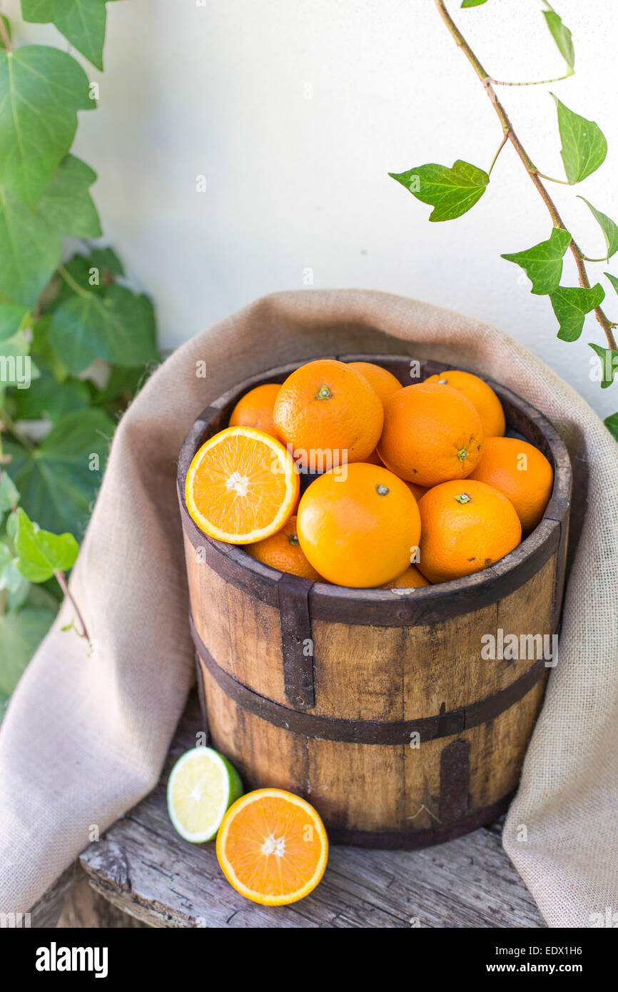 bucket of oranges, with sackcloth, on an old wooden bench against ivy covered white wall Stock Photo