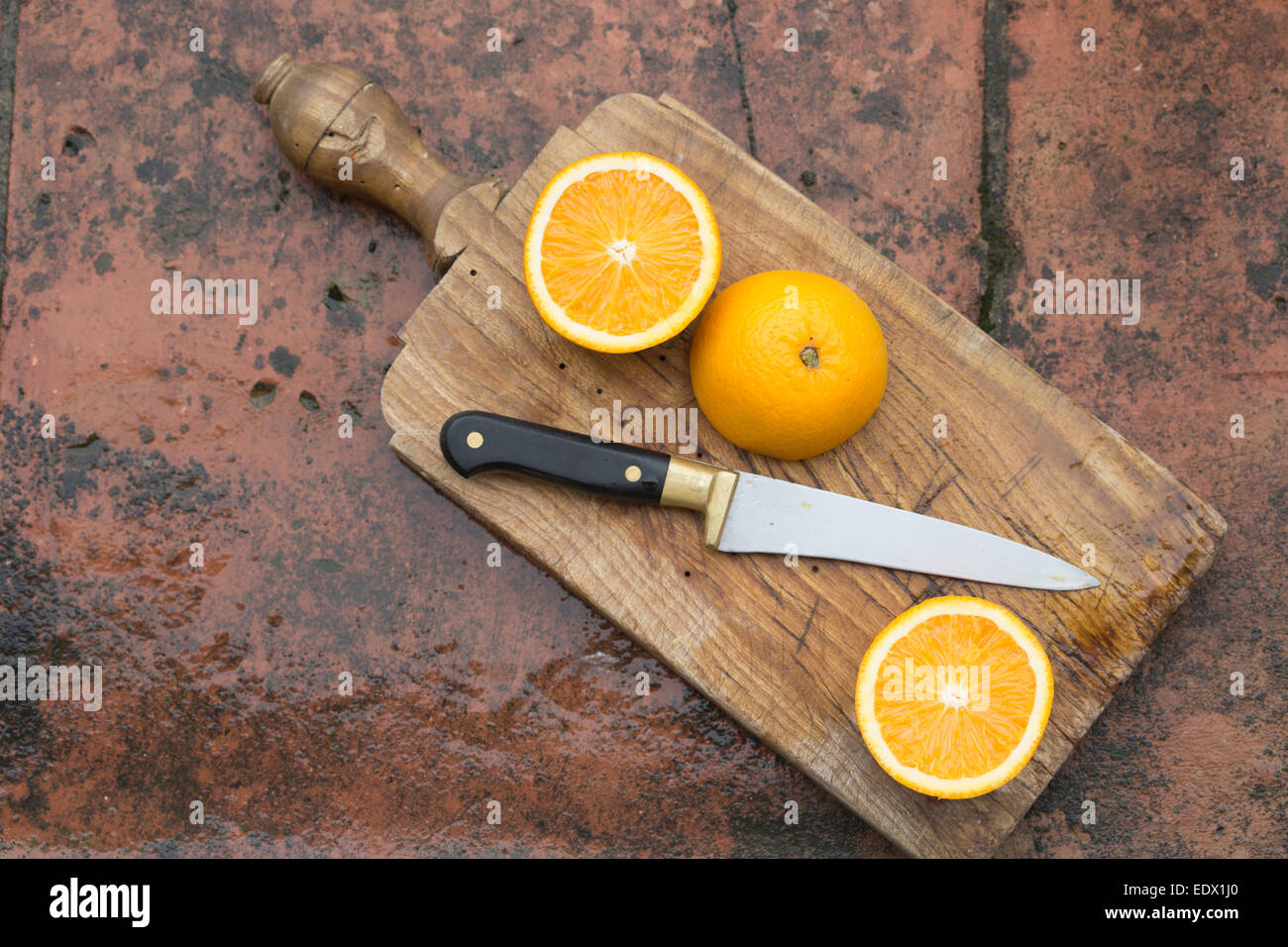 sliced oranges on an old wooden board with cutting knife, against terracotta tile wet surface background Stock Photo