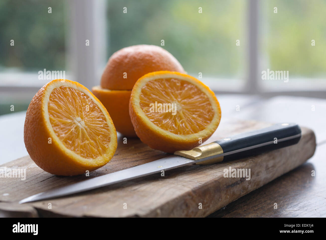 cut oranges on wood baord on table against window framed garden background Stock Photo