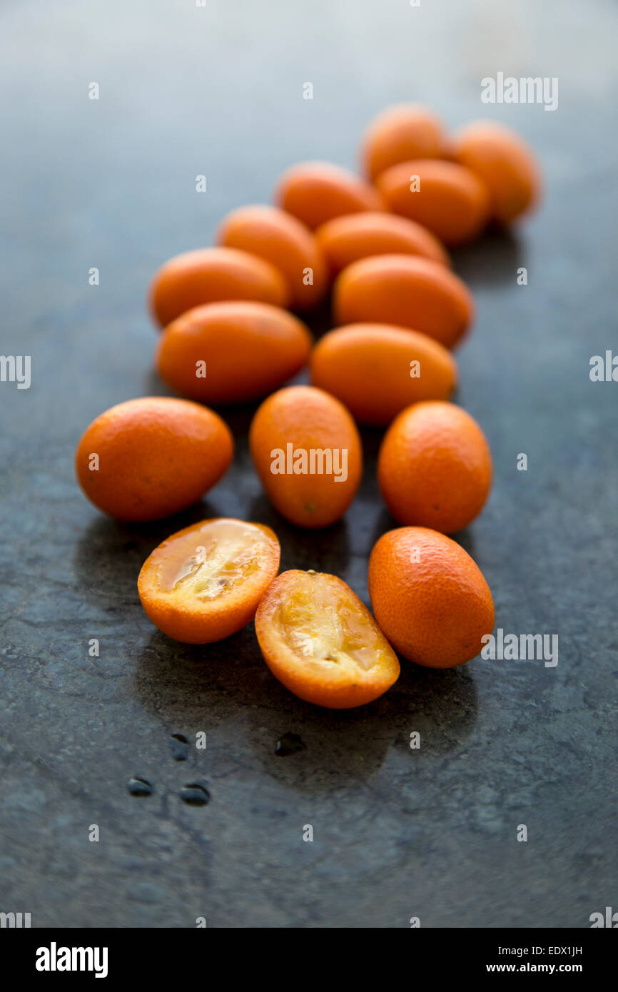 scattering of vibrant orange backlit kumquats, on green marble background Stock Photo
