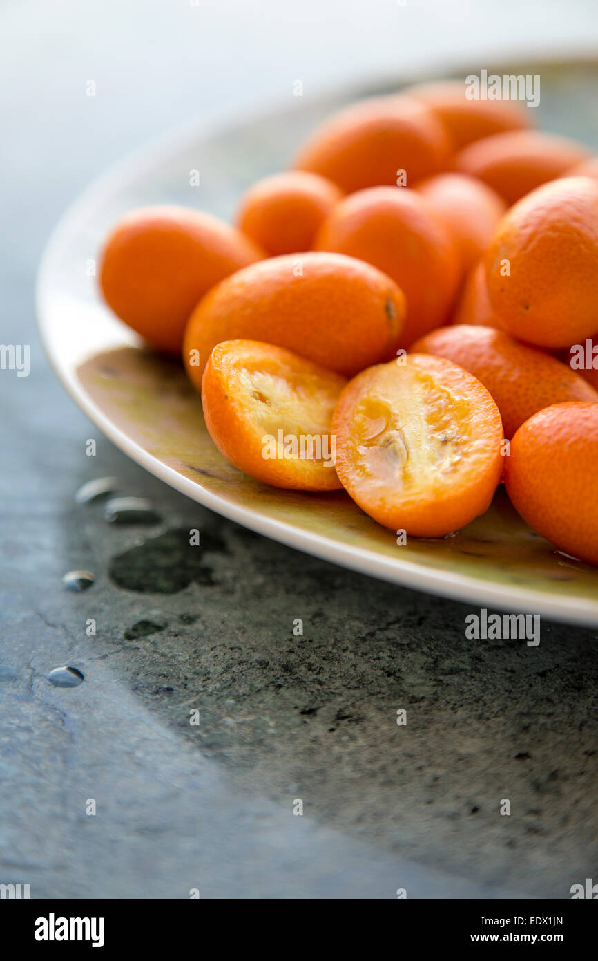 group of kumquats on a green plate on a green marble surface Stock Photo