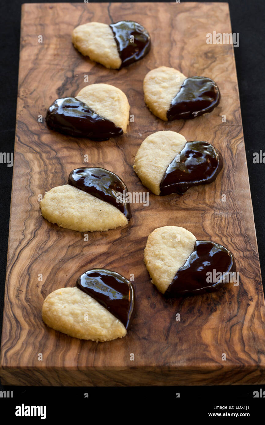 homemade chocolate dipped heart biscuits or cookies on olive wood board Stock Photo