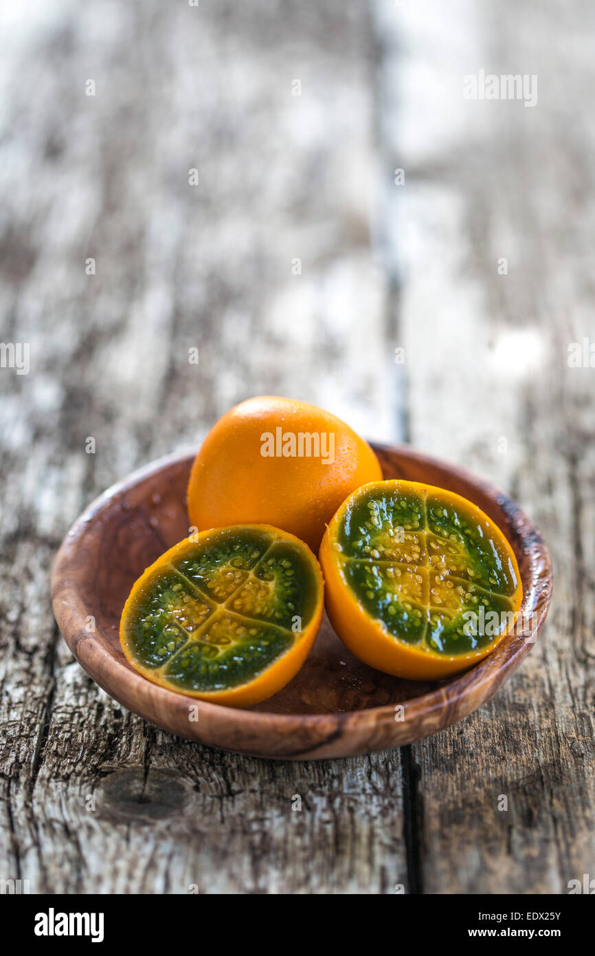 cut vibrant green and orange fleshed naranjilla in a wood bowl on rustic wood table Stock Photo
