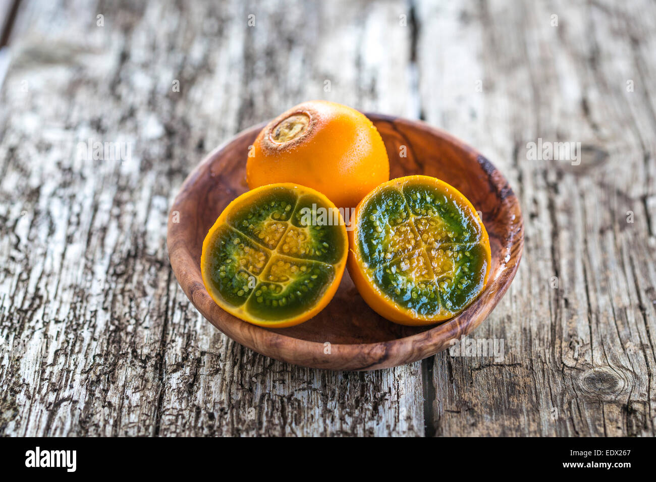 cut vibrant green and orange fleshed naranjilla in a wood bowl on rustic wood table Stock Photo