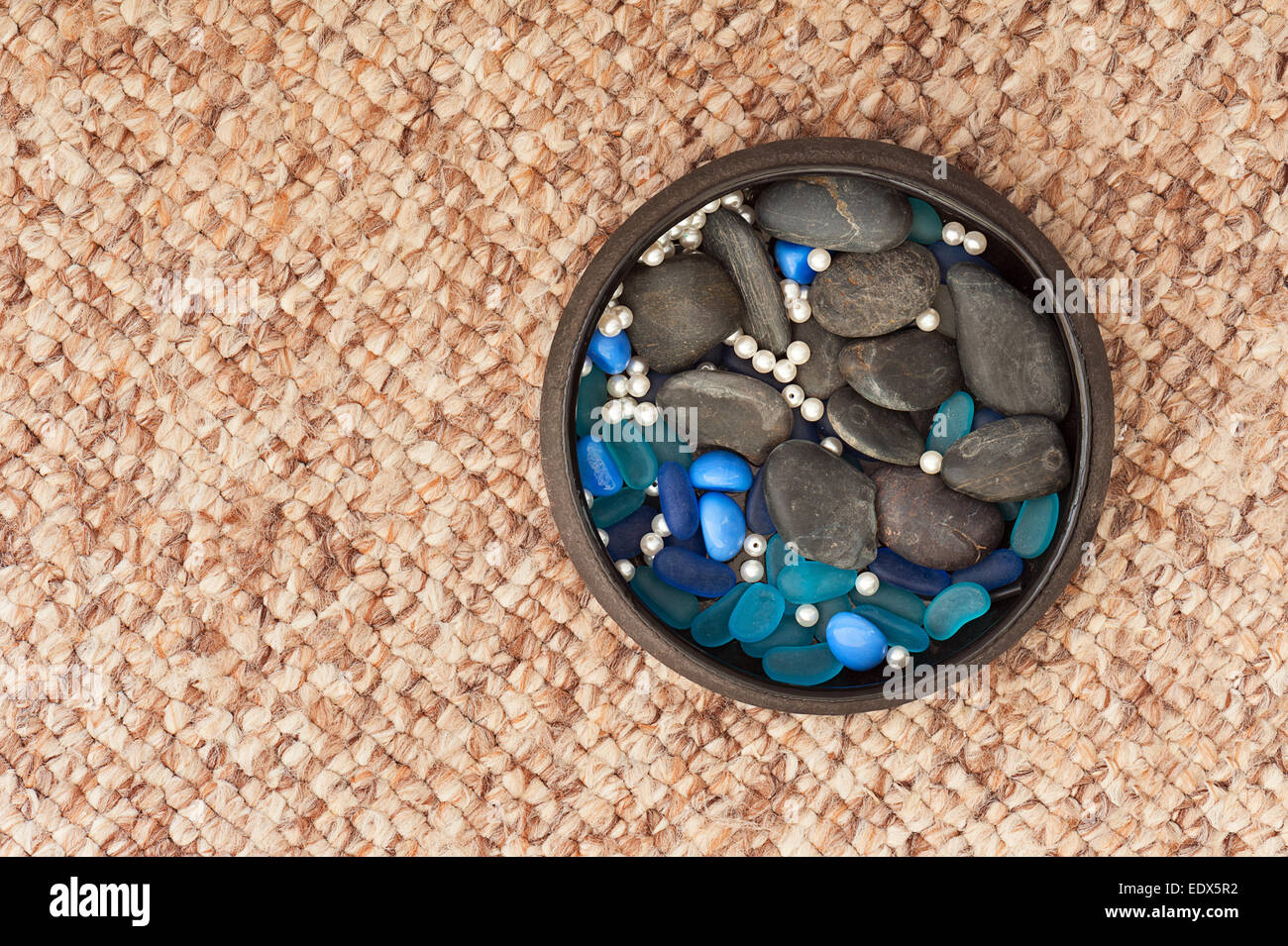 Pearls and colored stones in clay vase on carpet background. Closeup. Stock Photo