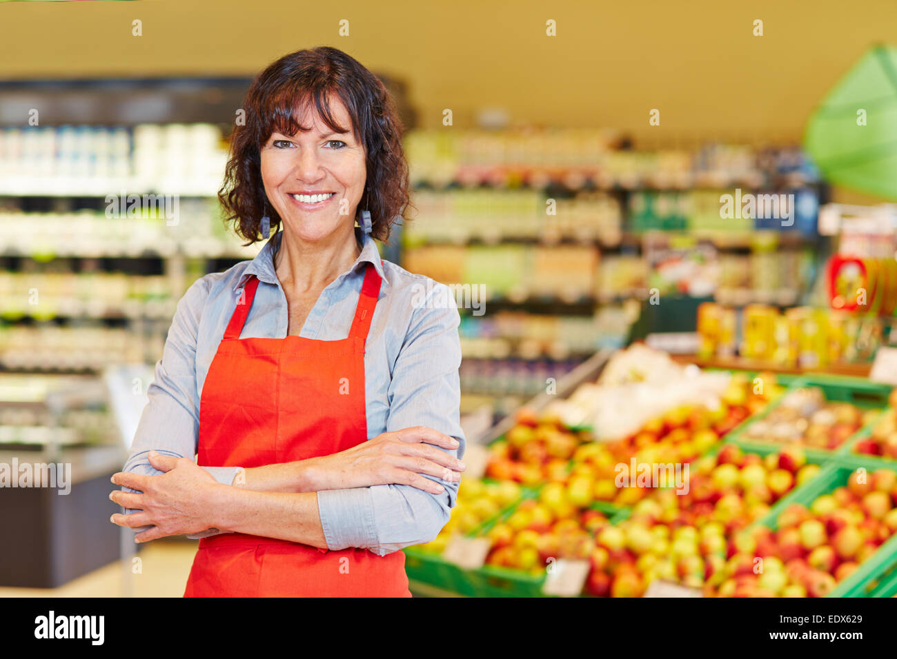 Elderly smiling saleswoman standing with her arms crossed in a supermarket Stock Photo