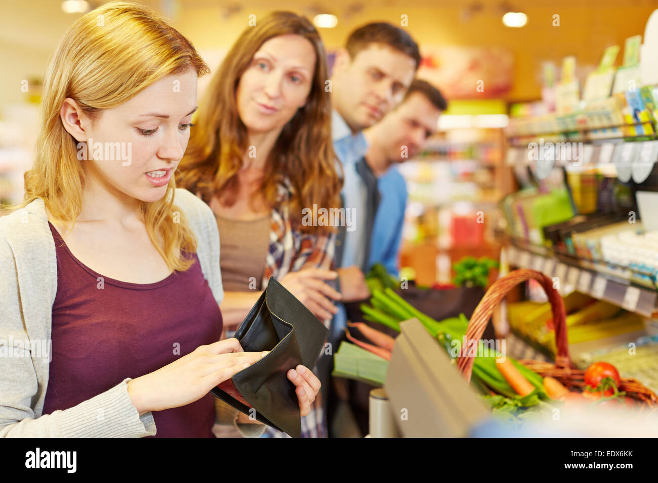 Embarrassed woman looking for money in her wallet at supermarket checkout Stock Photo