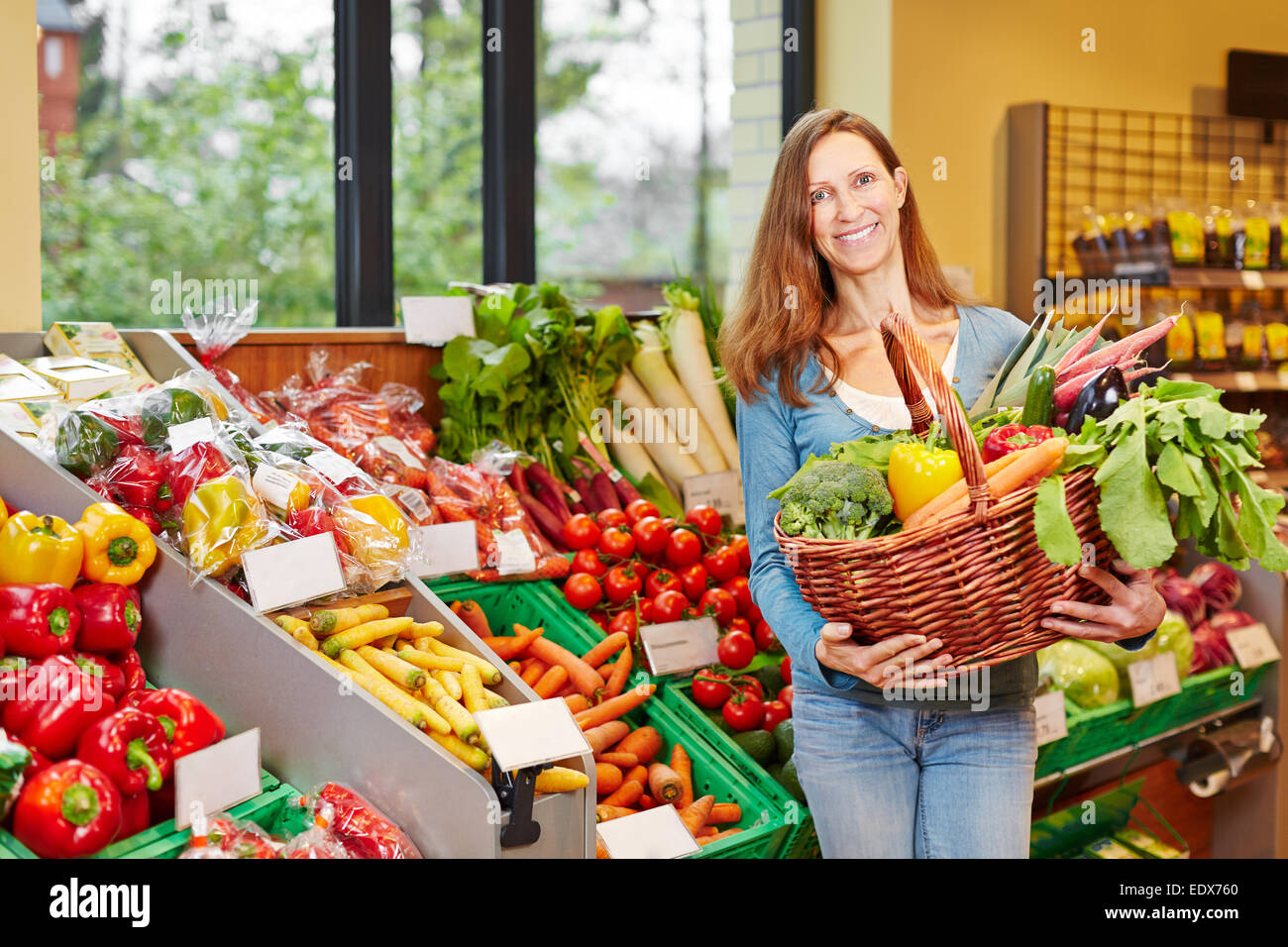 Smiling elderly woman holding basket with vegetables in organic food ...