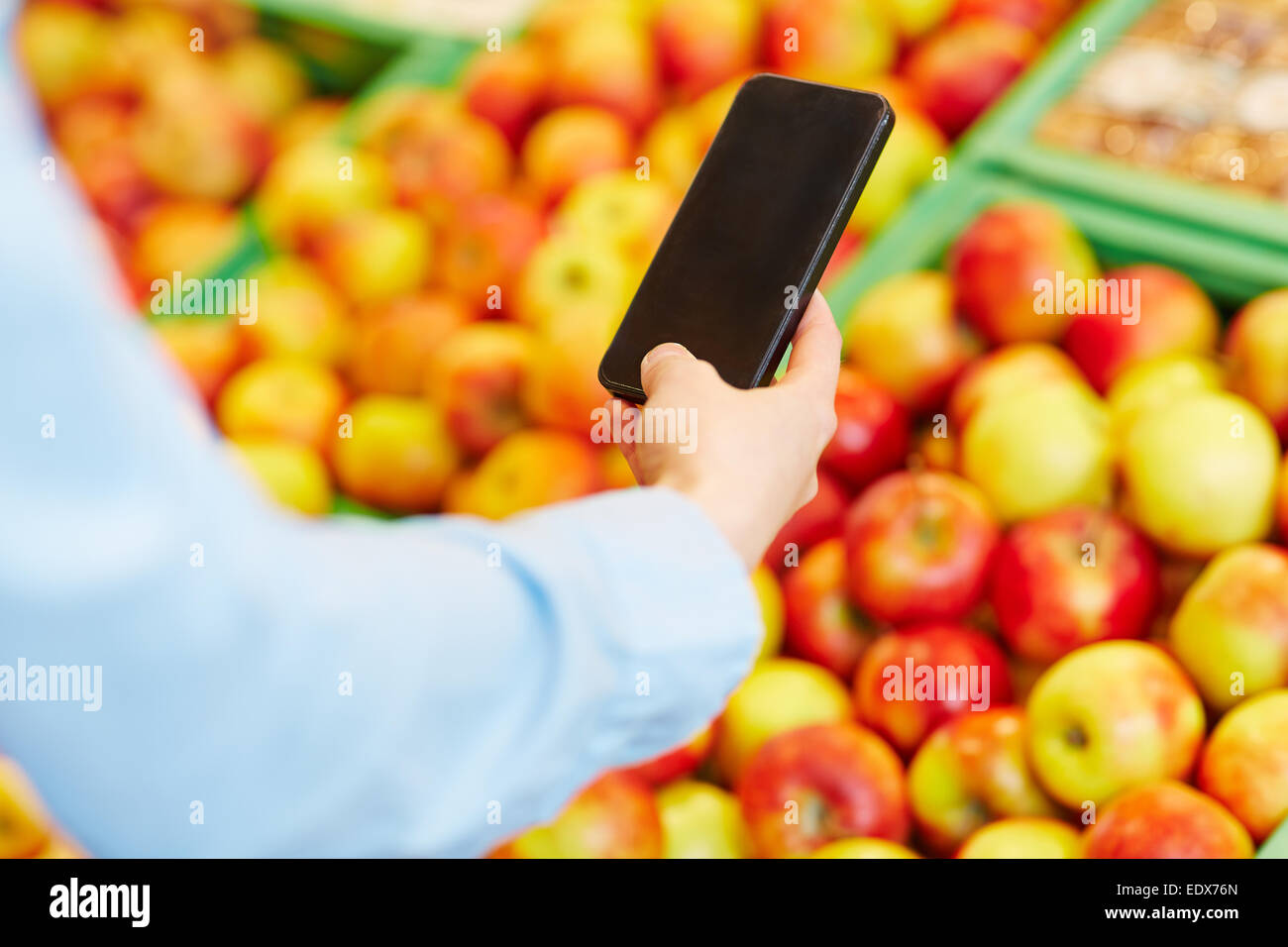 Male hand holding smartphone in front of fruits in a supermarket Stock Photo