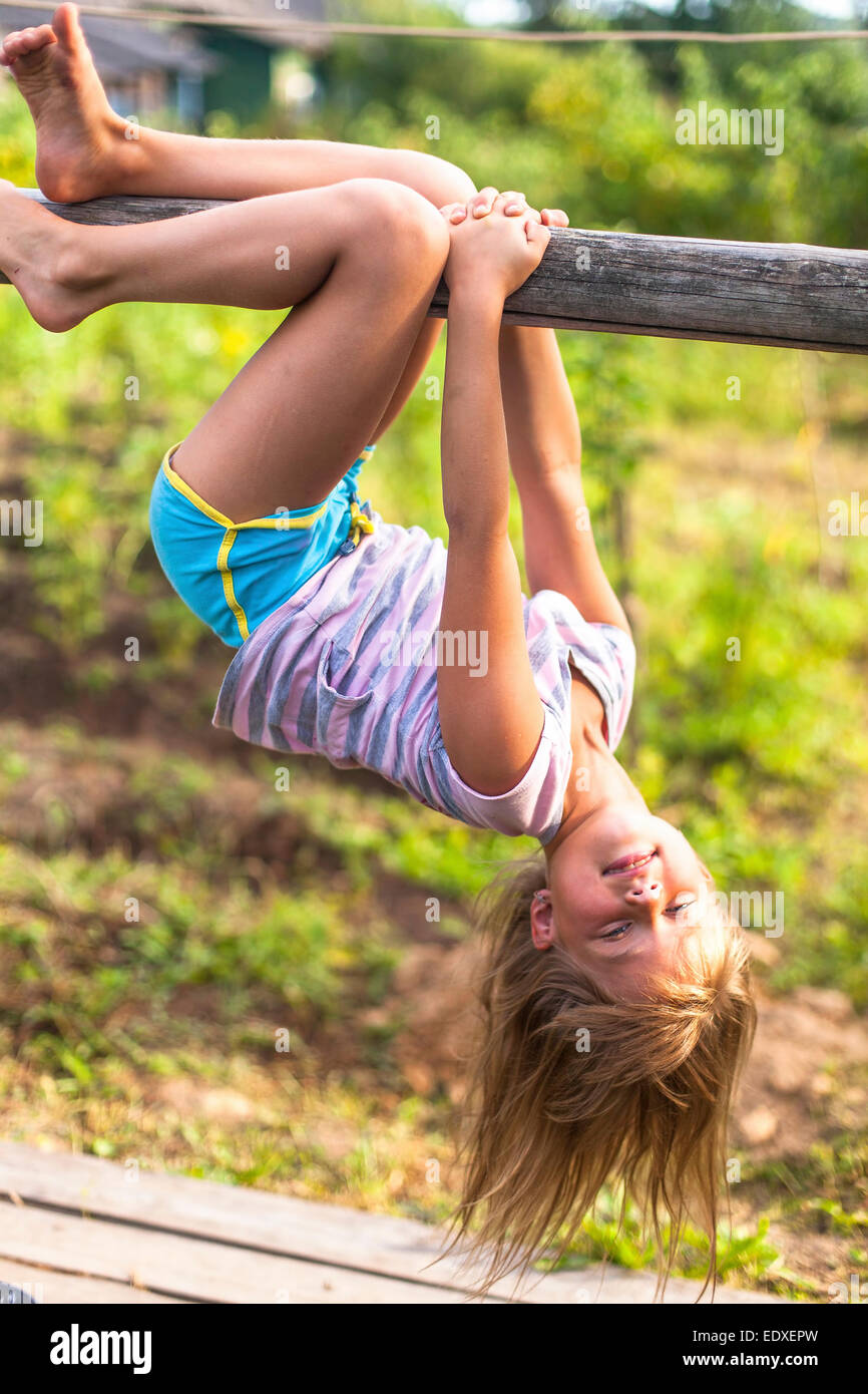 Little girl having fun in park hanging upside down on green rural countryside. Stock Photo