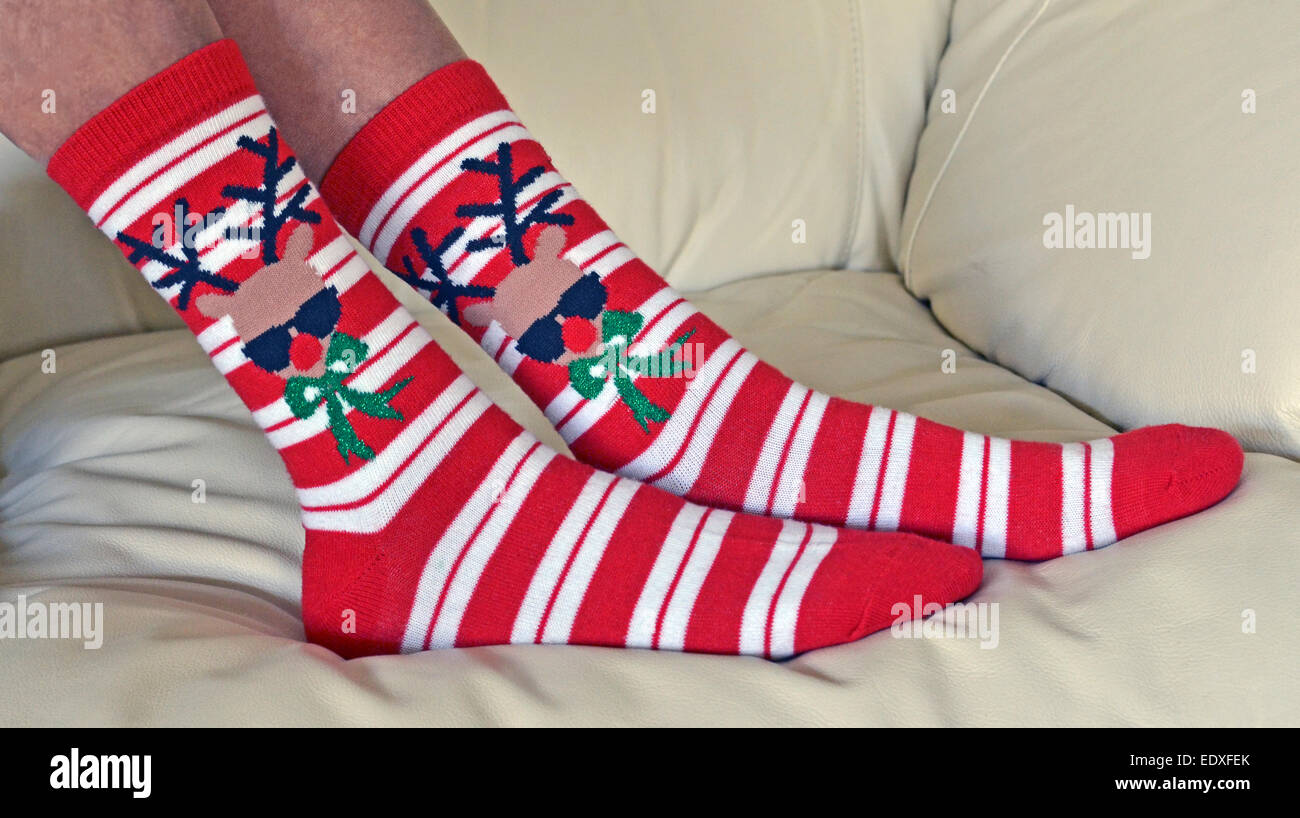 A pair of ladies red and white-striped Christmas socks is decorated with a contemporary red-nose reindeer wearing sunglasses and a fancy green bow tie Stock Photo