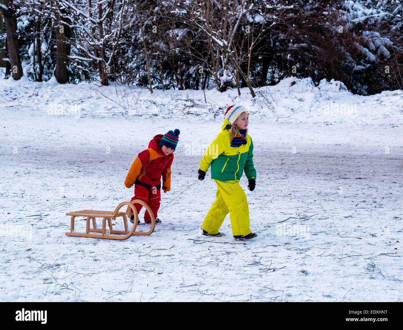 Two children in colourful clothing pull toboggan in snow covered Public