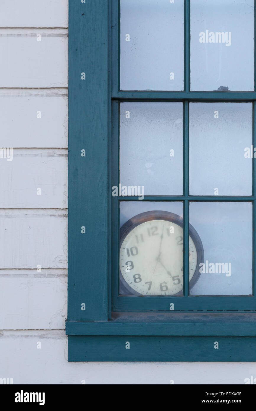 An old clock lies forgotten behind a window. Stock Photo