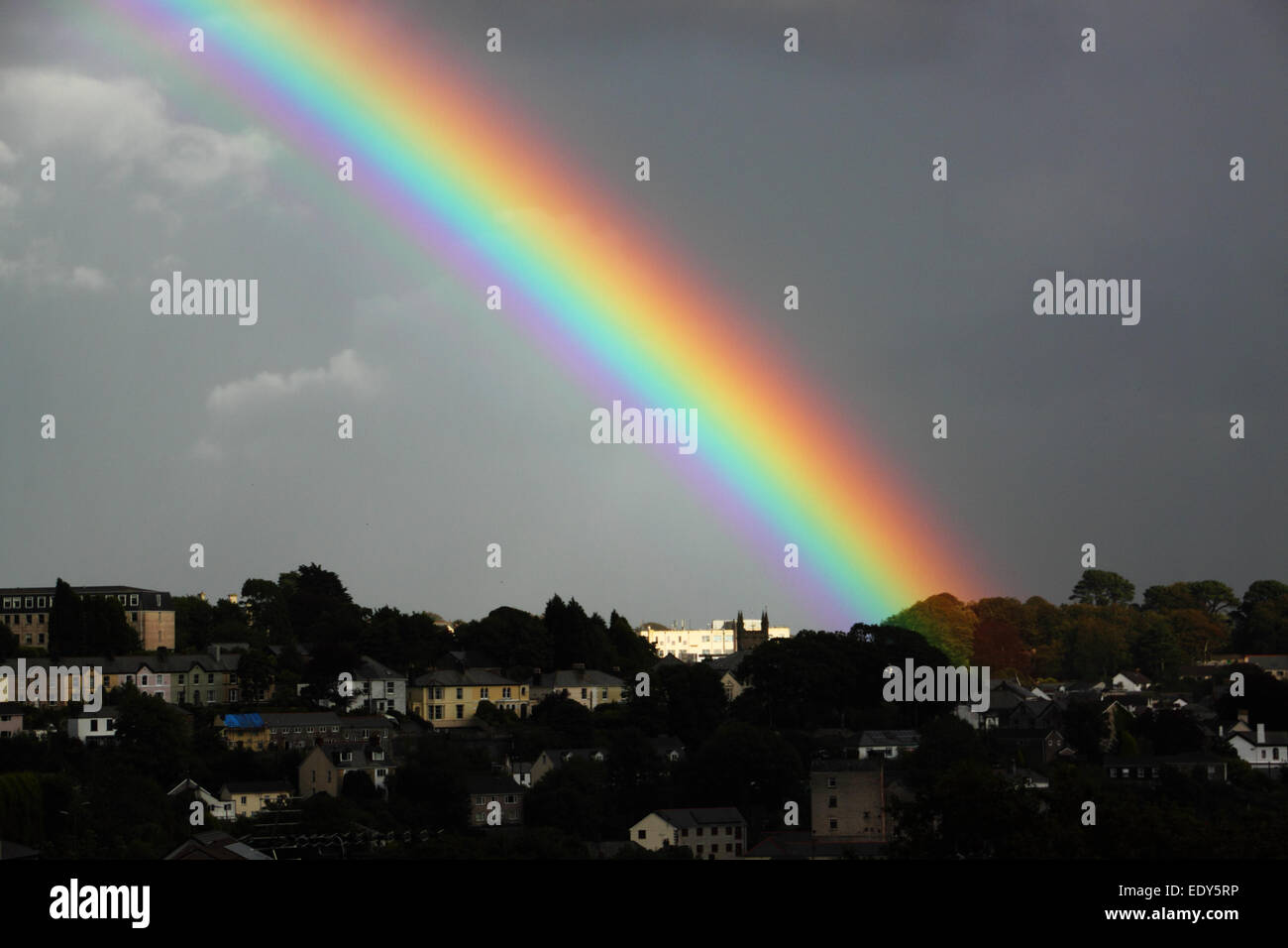A bright rainbow's end with dark clouds and buildings. Stock Photo