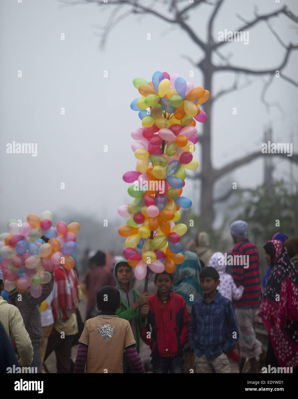 Dhaka, Bangladesh. 11th Jan, 2015. Bangladeshi boy carries balloons for sale as he watches Muslim devotees walk to attend the final prayer of the three-day Islamic Congregation on the banks of the River Turag in Tongi, 20 kilometers (13 miles) north of the capital Dhaka. Hundreds of thousands of Muslims attended the annual three-day event that is one of the world's largest religious gatherings being held since 1960's to revive Islamic tenets. It shuns politics and calls for peace. © Zakir Hossain Chowdhury/ZUMA Wire/Alamy Live News Stock Photo