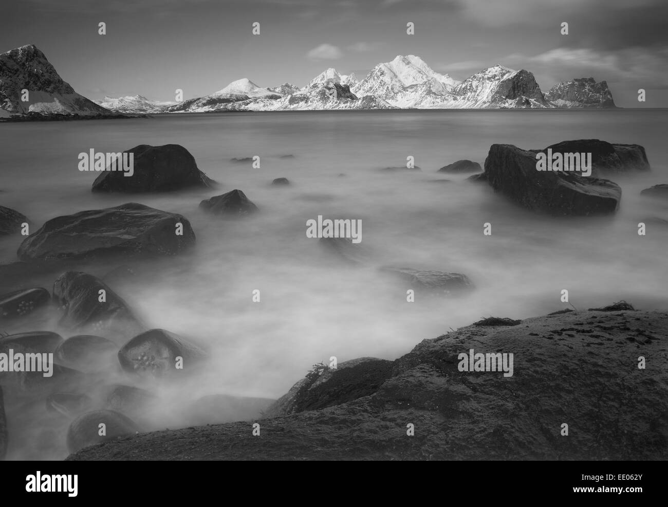 Long exposure of shoreline with rocky foreground and mountains in background in Lofoten Islands, arctic Norway. Stock Photo