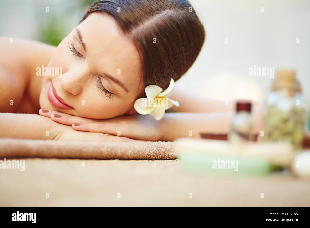 Relaxed female with frangipani flower in hair lying in spa salon Stock