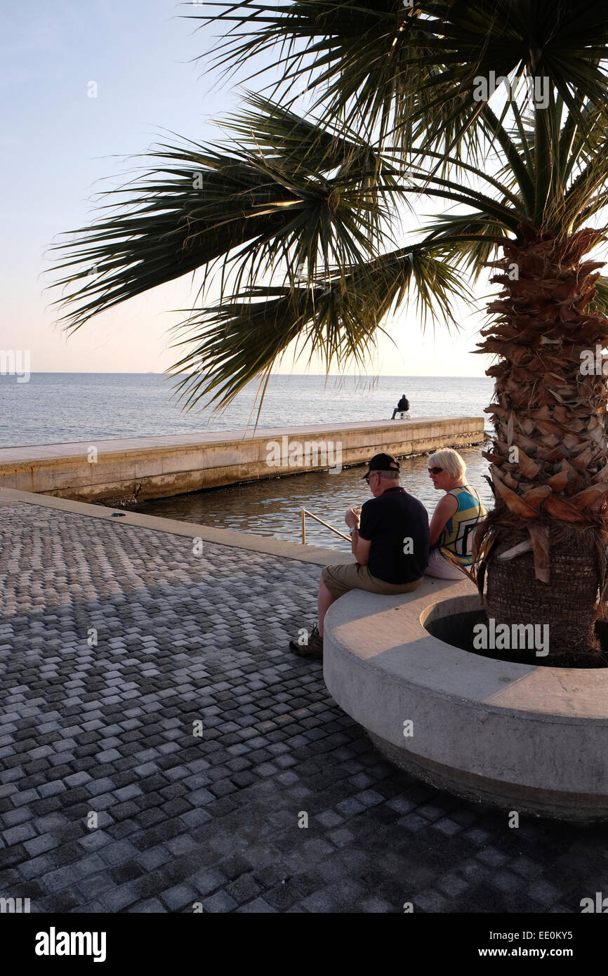 Quayside at Pafos, Western Cyprus, with couple eating ice cream and man fishing Stock Photo